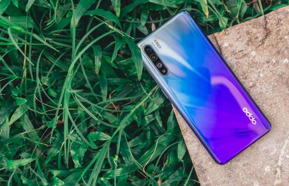  A sleek Oppo Reno Series smartphone with a pop-up selfie camera and a gradient color design is placed on a granite slab and grass in the background.