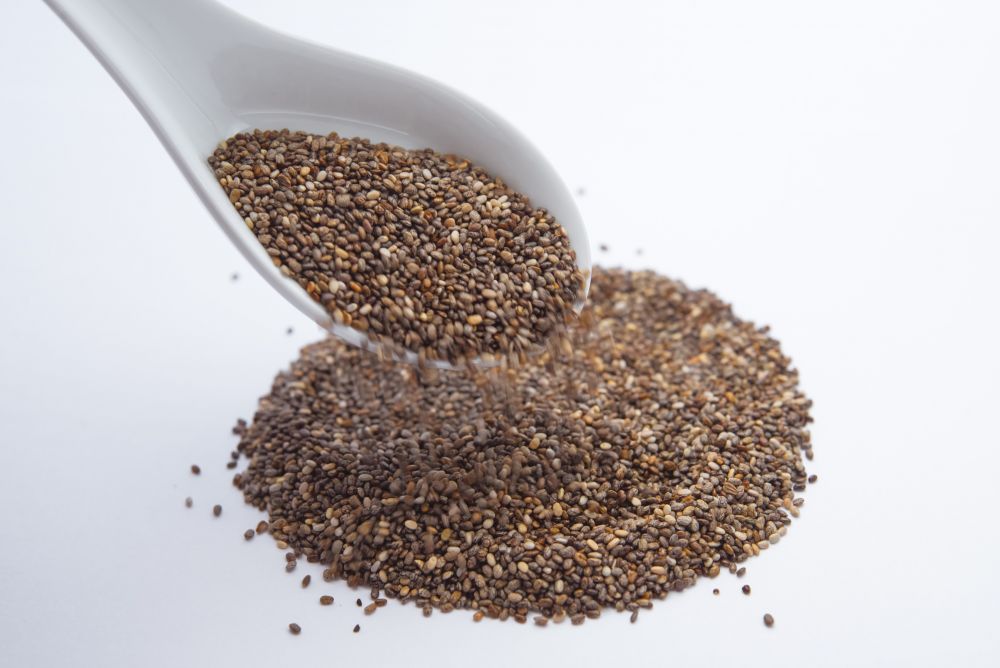  A pile of chia seeds with a white spoon hovering above it.