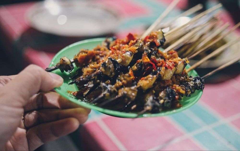 Gambar Sate Kolombi khas Sulawesi Utara yang disajikan dengan bumbu rempah merah, terlihat lezat dan unik dengan tusukan keong rawa yang kenyal