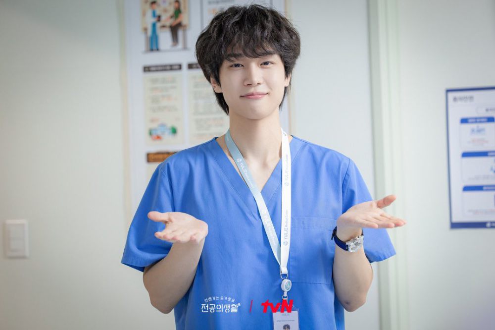Karakter Resident Playbook, Um Jae-il, memakai scrub biru khas dokter sambil menengadahkan tangannya